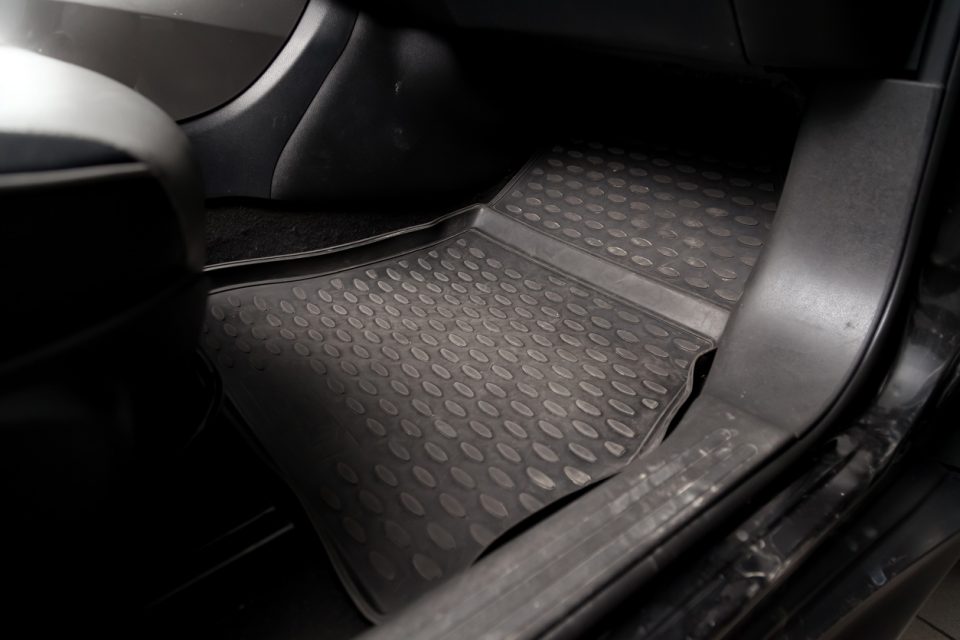 Dirty car floor mats of black rubber under passenger seat in the workshop for the detailing vehicle before dry cleaning. Auto service industry. Interior of sedan.