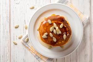Pumpkin pancakes with honey and pumpkin seeds in plate on white wooden background.