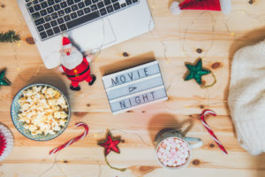 Top view Christmas Movie night concept. Flat lay composition with Movie night message on the board, laptop, popcorn bowl, decor, a cup of cocoa with marshmallows and warm plaid on wooden background.