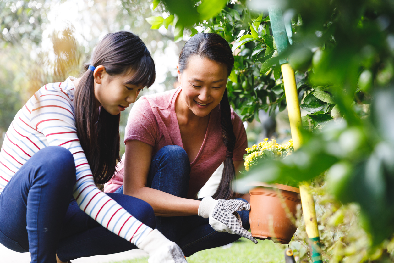 mother and daughter smiling, wearing gloves and working in garden