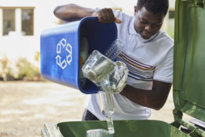 Young Man Emptying Household Recycling Into Green Bin
