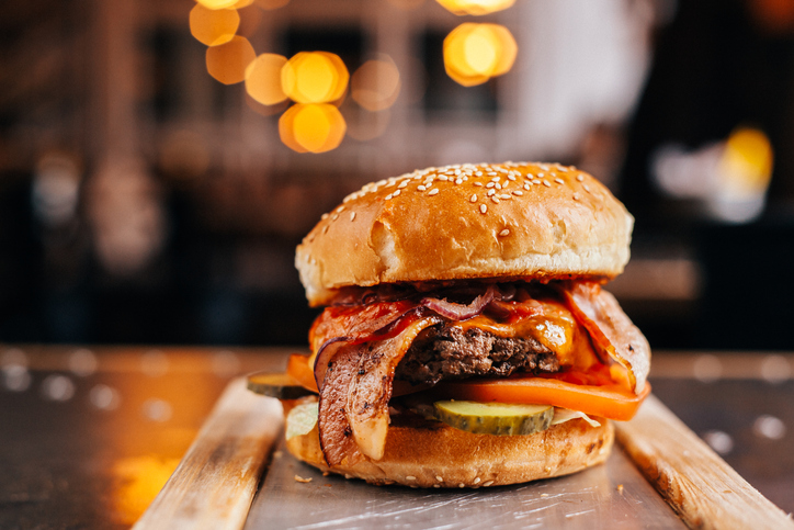 Burger with a cutlet of murbled beef with cheddar cheese, bacon, spicy chili sauce, cucumber and tomato, in a white bun with sesame seeds served