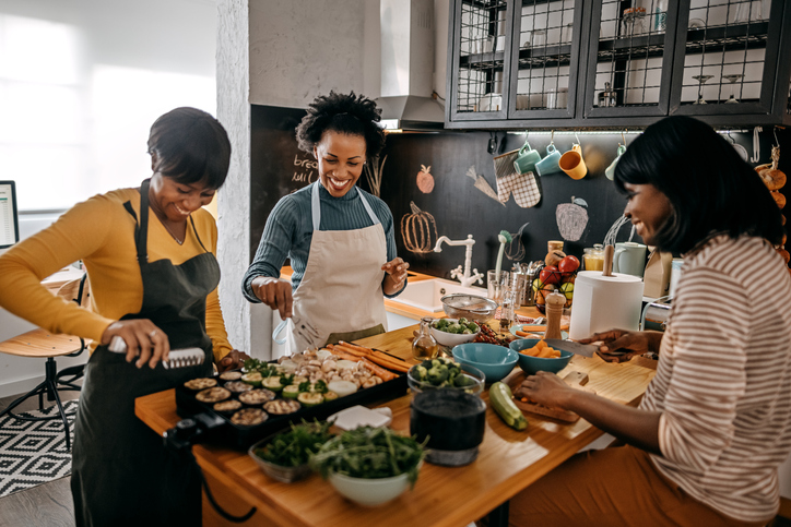 Three happy female friends preparing food in domestic kitchen for thanksgiving celebration