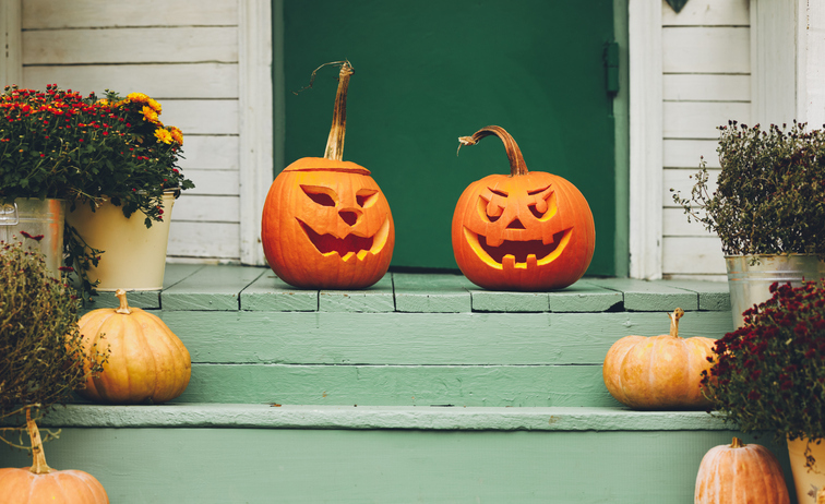 Staircase autumn decor. House entrance with halloween pumpkin decoration on wooden stairs, two jack o lanterns with spooky faces on porch of apartment building during all hallows eve