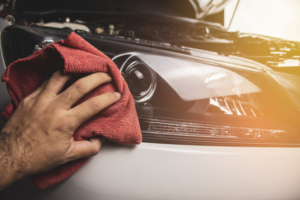 Hand is cleaning car headlight using a red microfiber cloth.