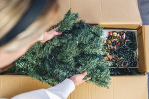 Young woman unpacked the Christmas Tree box and taking out the Christmas Tree from the cargo box in the her living room.