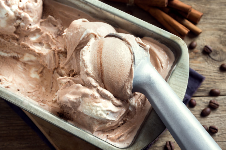 Homemade ice cream with scoop in frozen metallic container on wooden background